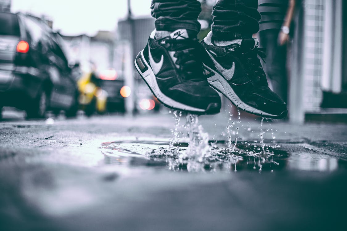 Free Black sneakers splashing water in city street, capturing youthful energy and urban lifestyle. Stock Photo