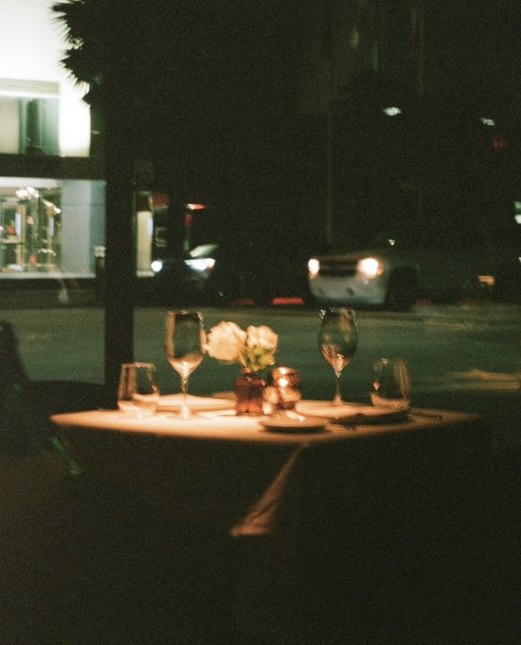 This may contain: a table with wine glasses and flowers on it in the middle of a street at night
