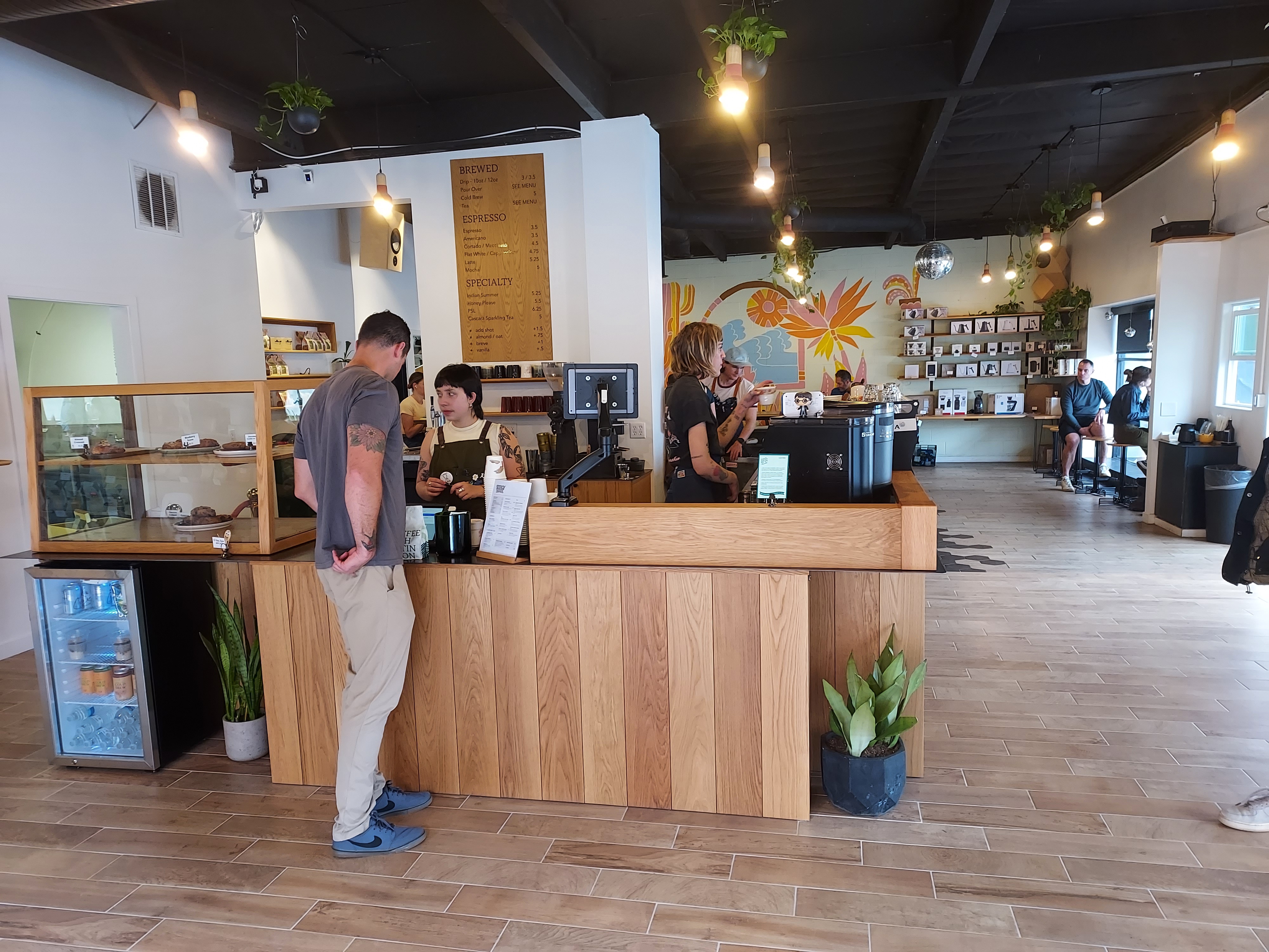 A gentleman orders coffee from a barista in a bright coffee shop.