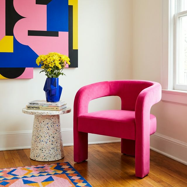 FunHaus living room vignette with a sculptural Rebel Pink velvet accent chair, terrazzo side table, cobalt blue geometric vase with yellow flowers, Memphis art books, and bold geometric abstract wall art