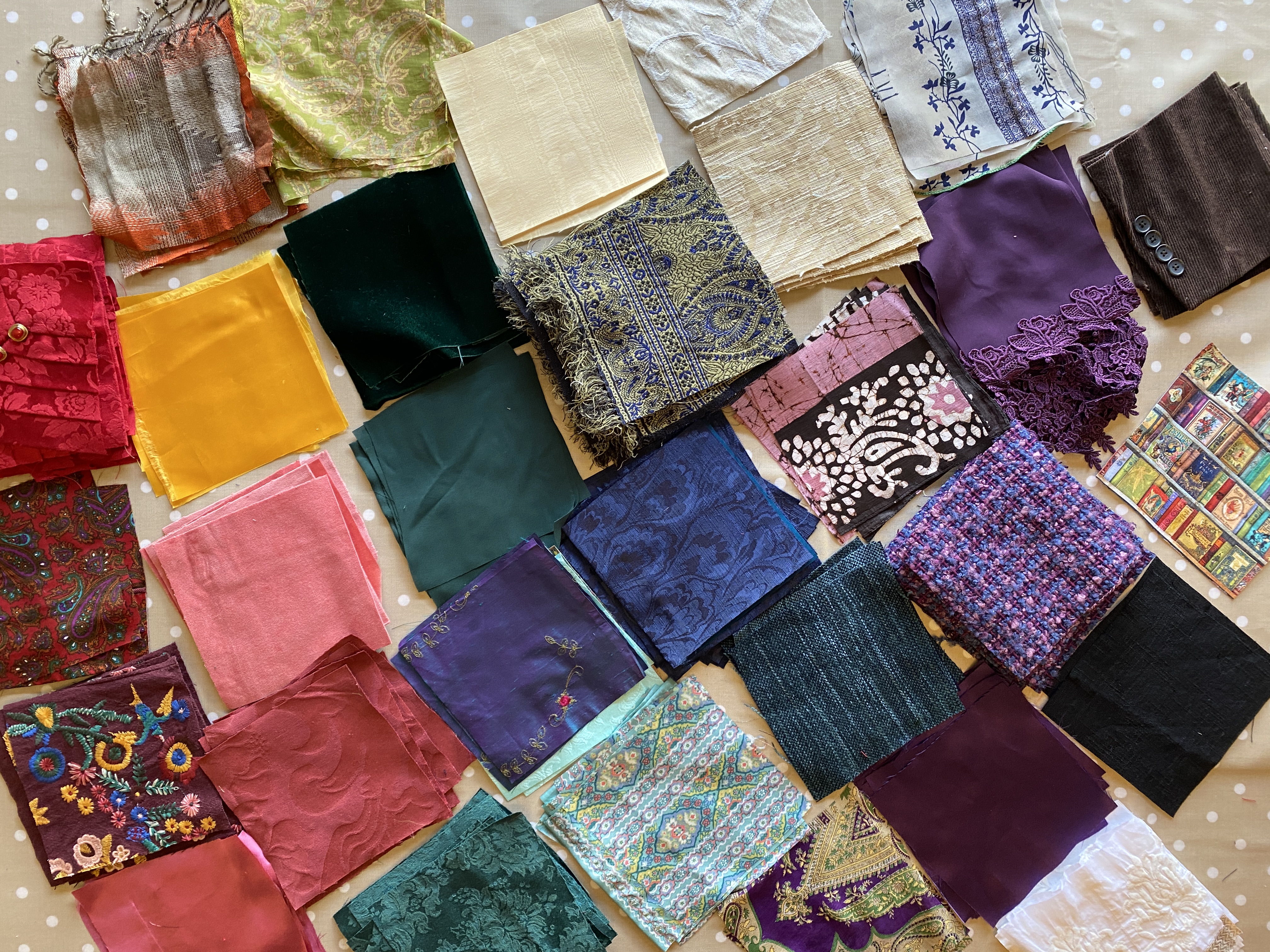 Piles of 209 square patches sorted by colors: red, gold, yellow, blue, green, purple, white, brown, black. There are also various textures: velvets, brocade, silk, corduroy, satin, batik, embroidered, and a red pleated satin with a row of red and gold buttons.