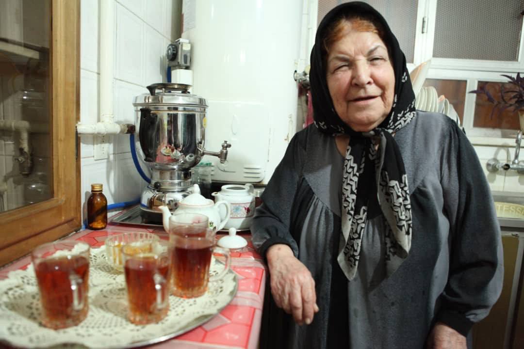 Older woman beside a samovar and glasses of tea in a kitchen