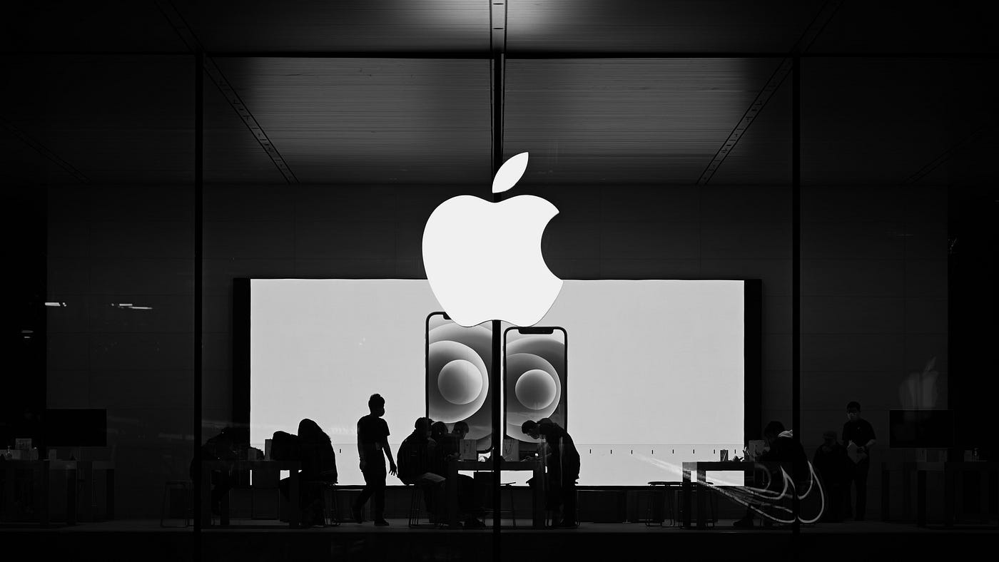 Black-and-white photo of people working inside an Apple Store under the glowing Apple logo, showcasing minimalist design and brand coherence.