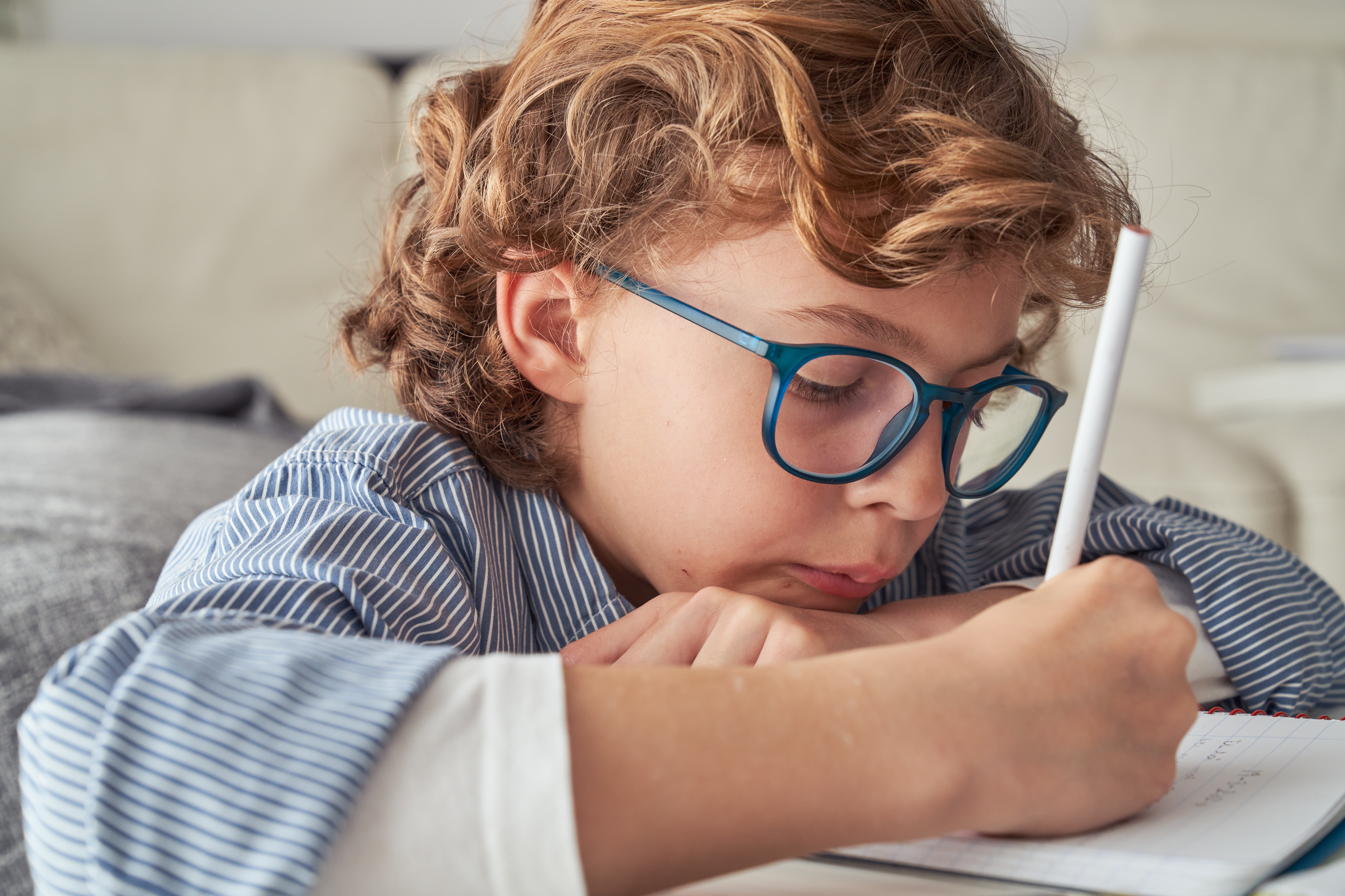 Focused boy writing notes in notepad with pencil at home