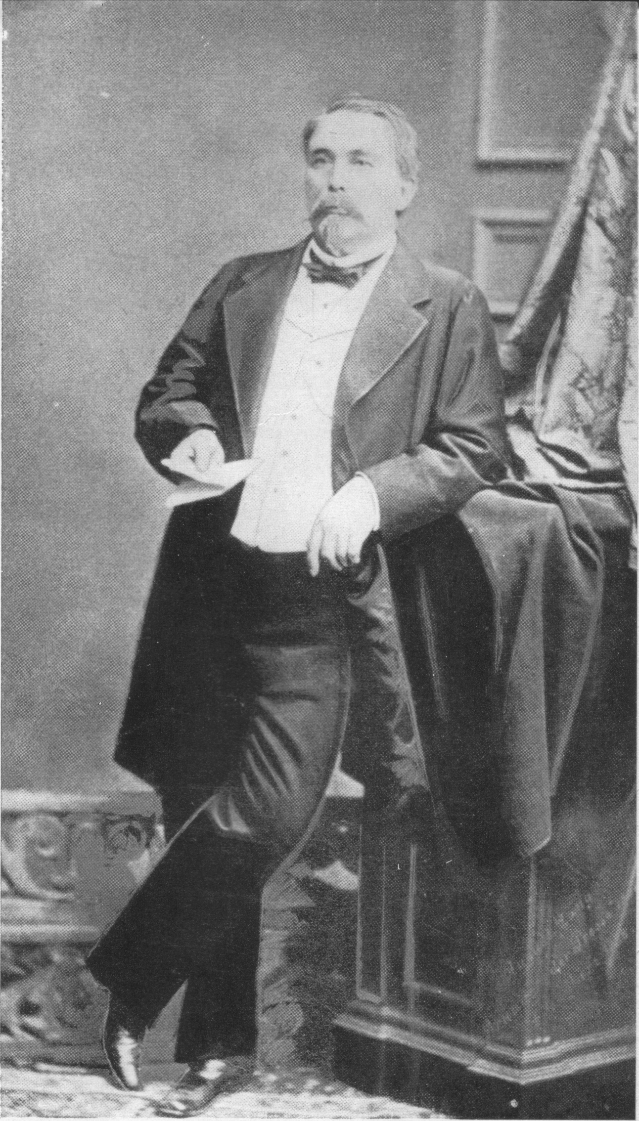 Historic black-and-white studio portrait of a seated man in a dark suit