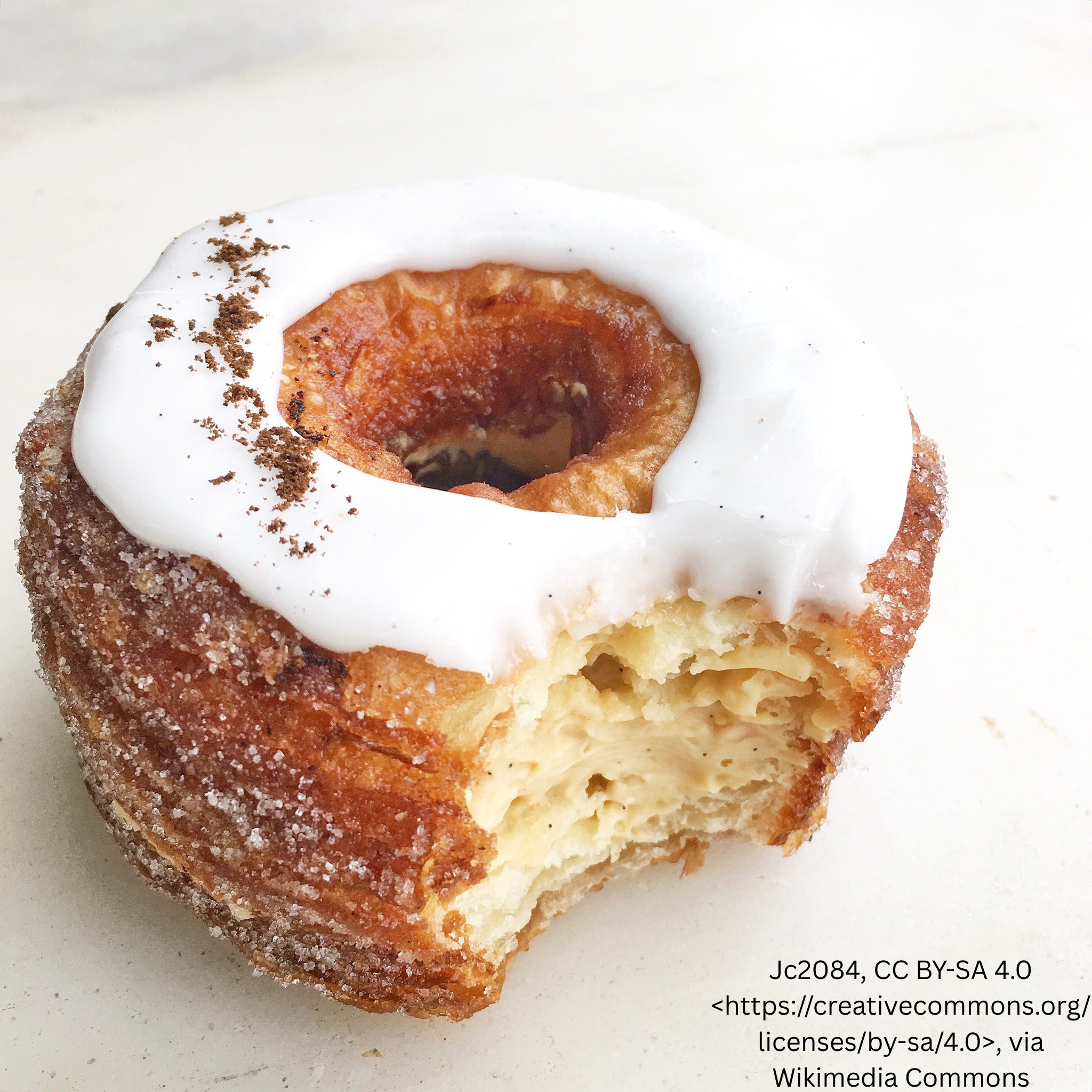 Iced cronut with a bite taken out, showing its layered interior