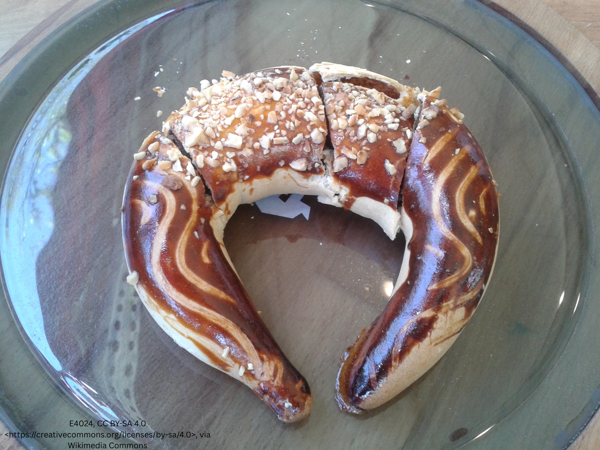 Horseshoe-shaped glazed pastry topped with chopped nuts on a glass plate