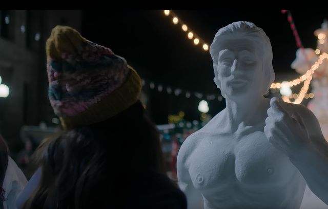 Kathy standing in front of a muscled snowman, at night.