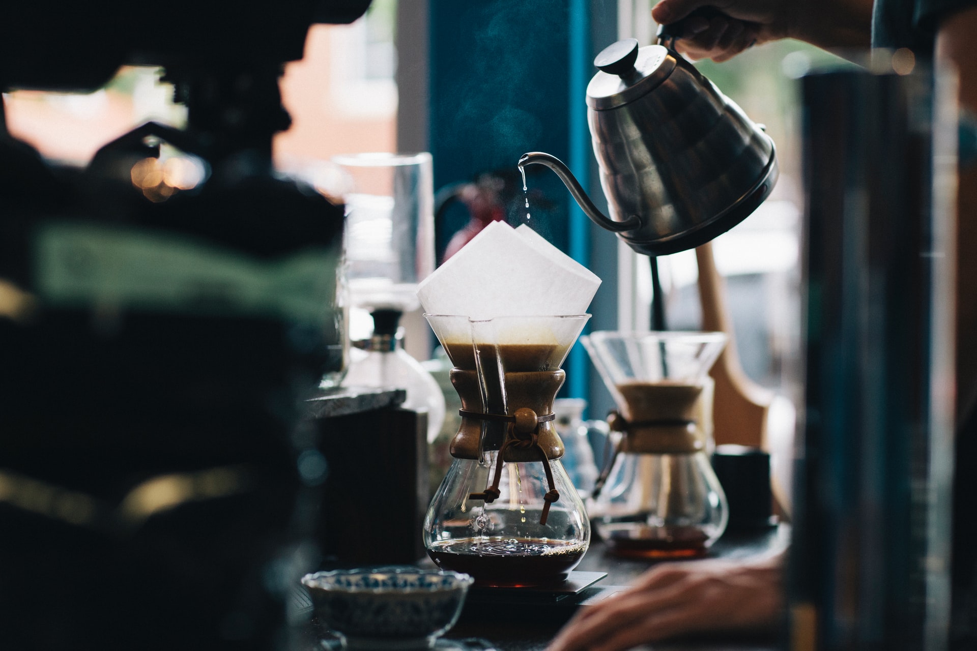 A coffee roaster pouring hot water into a chemex coffee brewer.