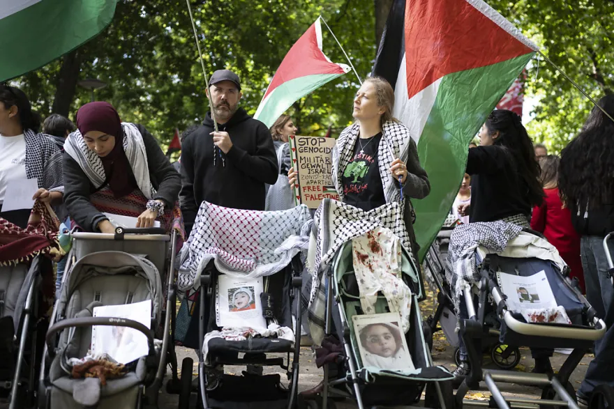 A diverse group of people push empty prams with images of murdered gazan children. They stand in front of a crowd of thousands. A diverse group of people push empty prams with images of murdered gazan children. They stand in front of a crowd of thousands.