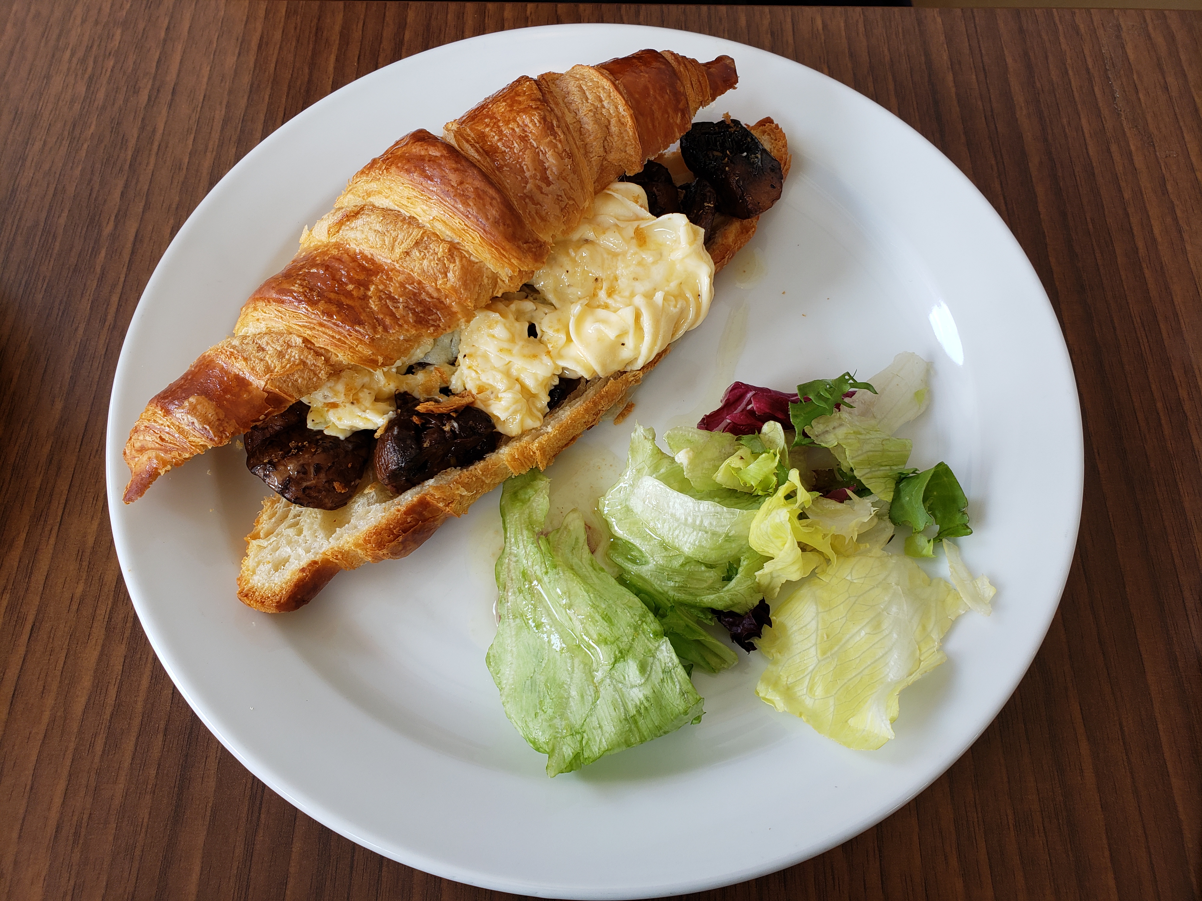 Croissant sandwich filled with eggs and meat beside a green salad