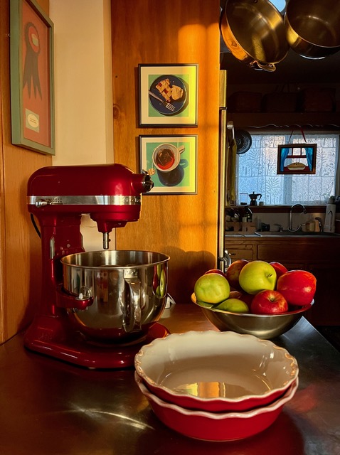 Red food mixer and dishes of fruit on a counter top.