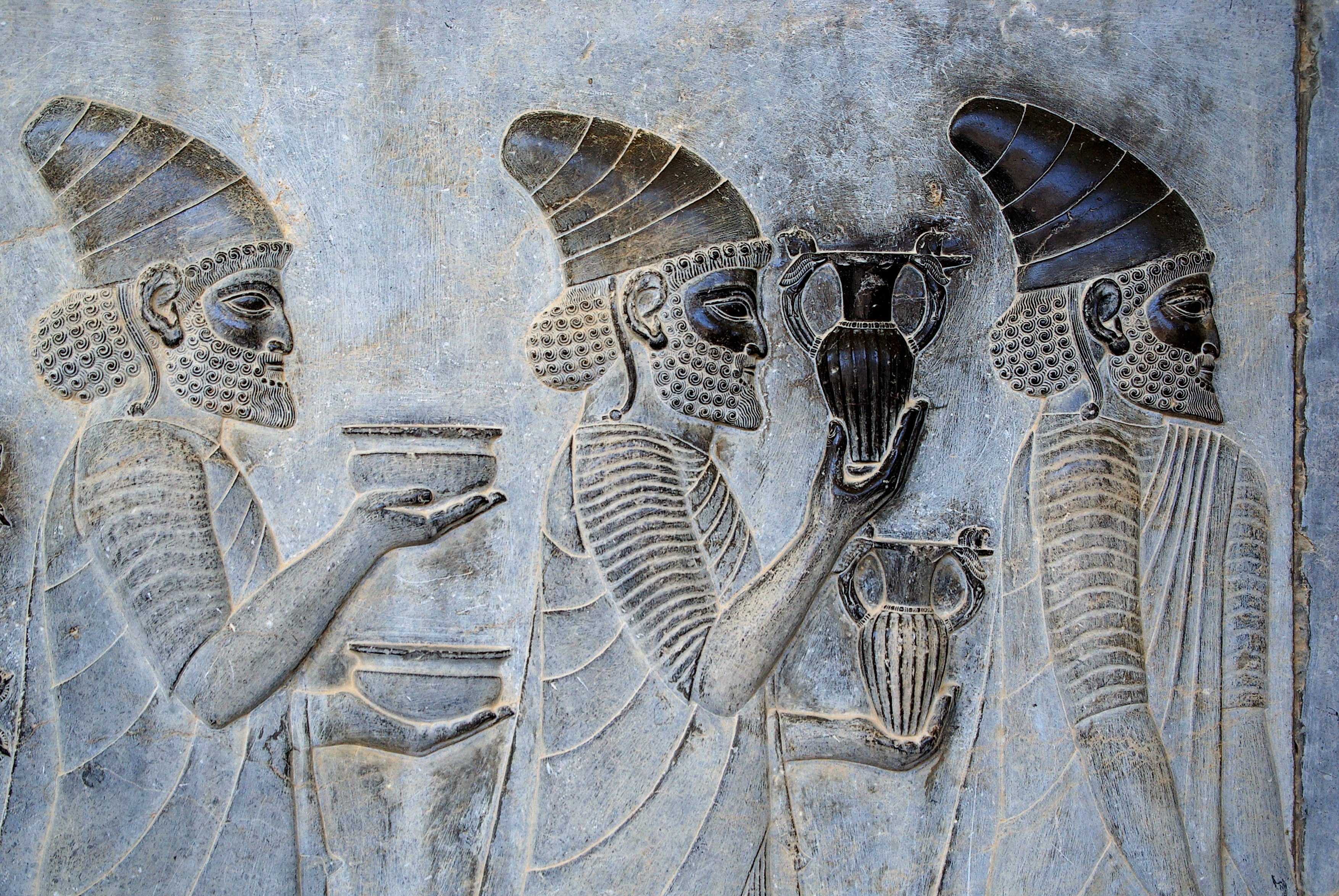 Ancient Persian stone relief of figures carrying vessels and gifts