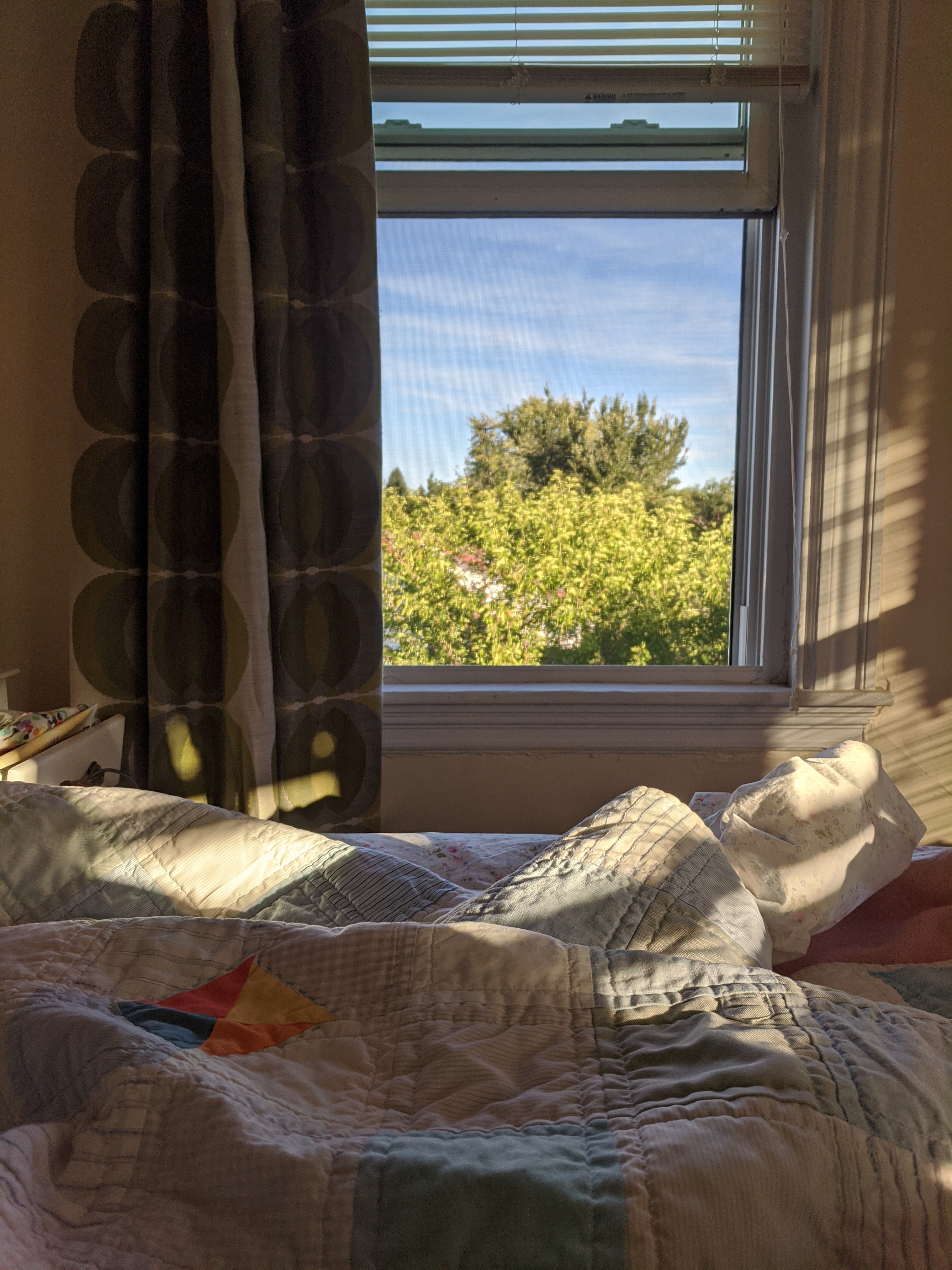 A wide-open screen window. A bed covered in rumpled quilts is in front of it.
