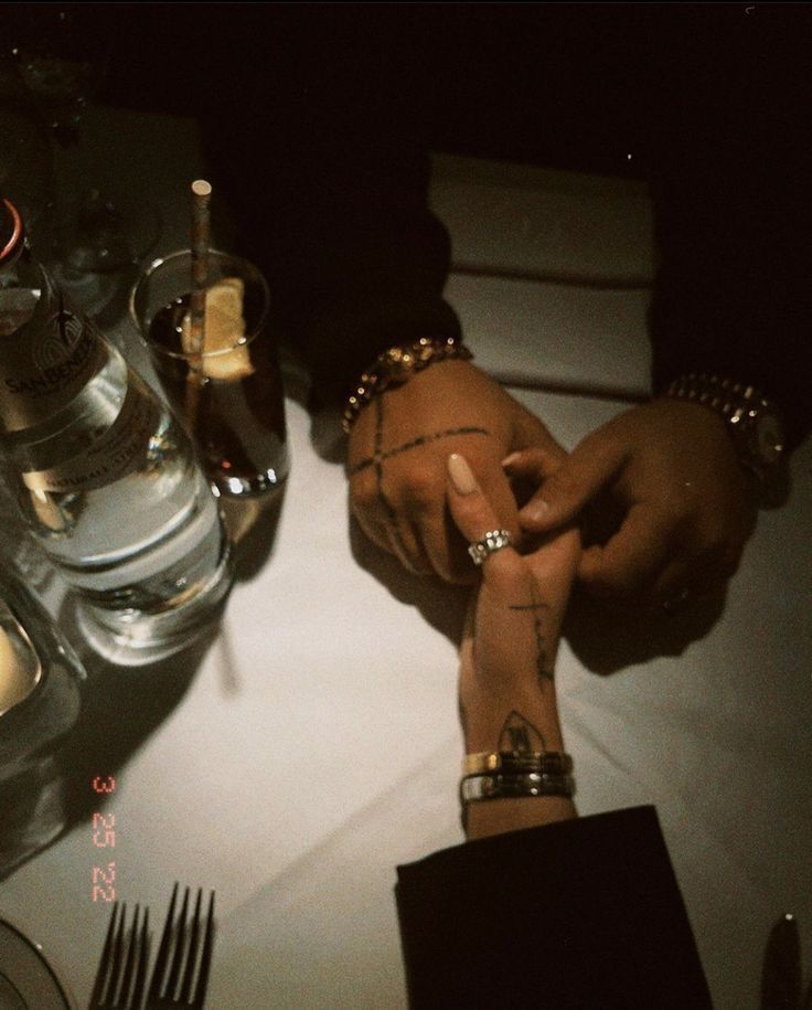 This may contain: two people sitting at a table with their hands on each other's wrists