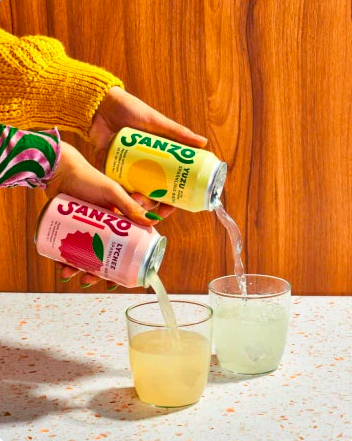 Two hands pour cans of sanzo into two glasses. 