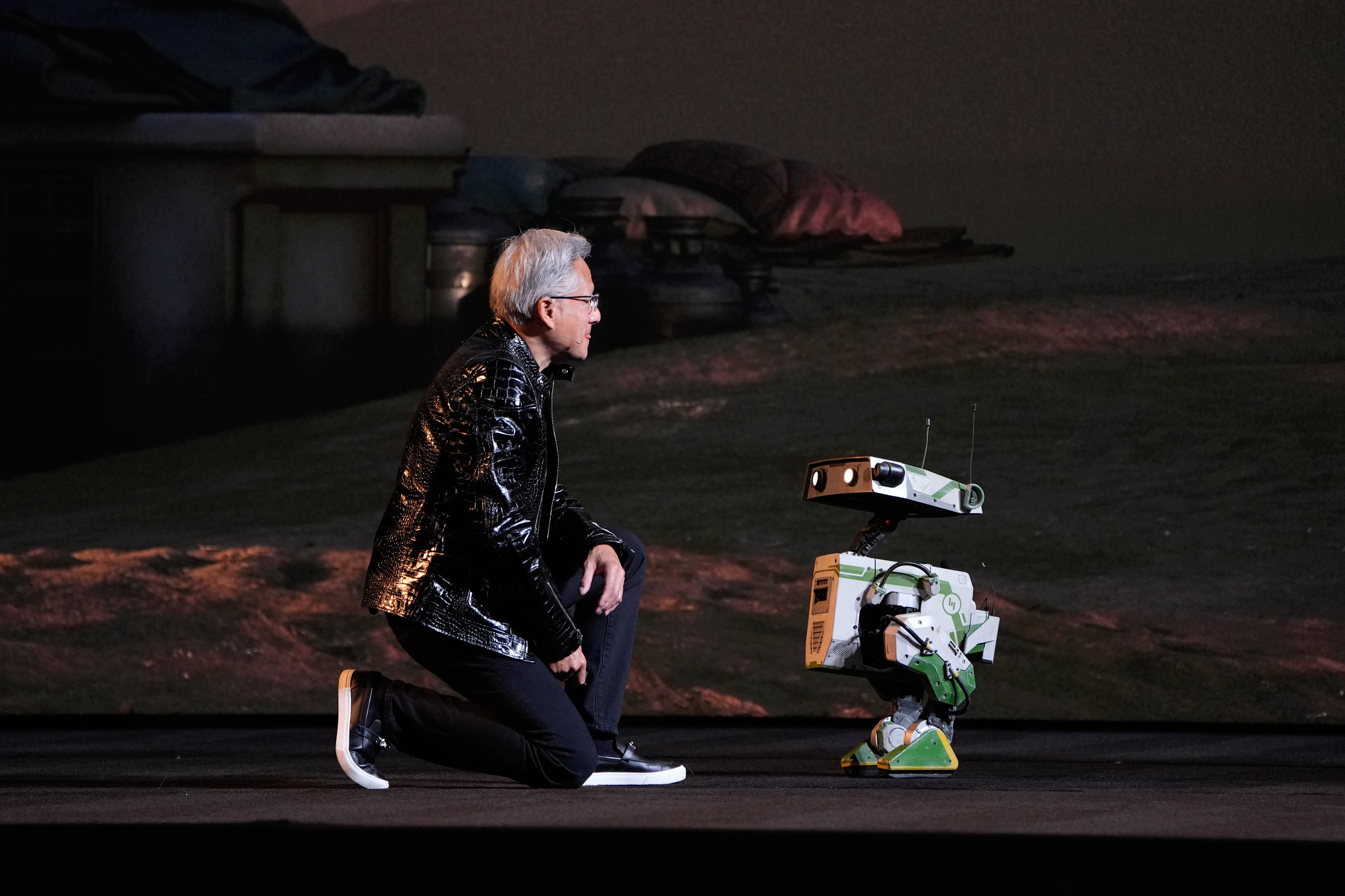 Nvidia founder and CEO Jensen Huang kneels in front of a robot during a Nvidia news conference ahead of the CES tech show Monday, Jan. 5, 2026