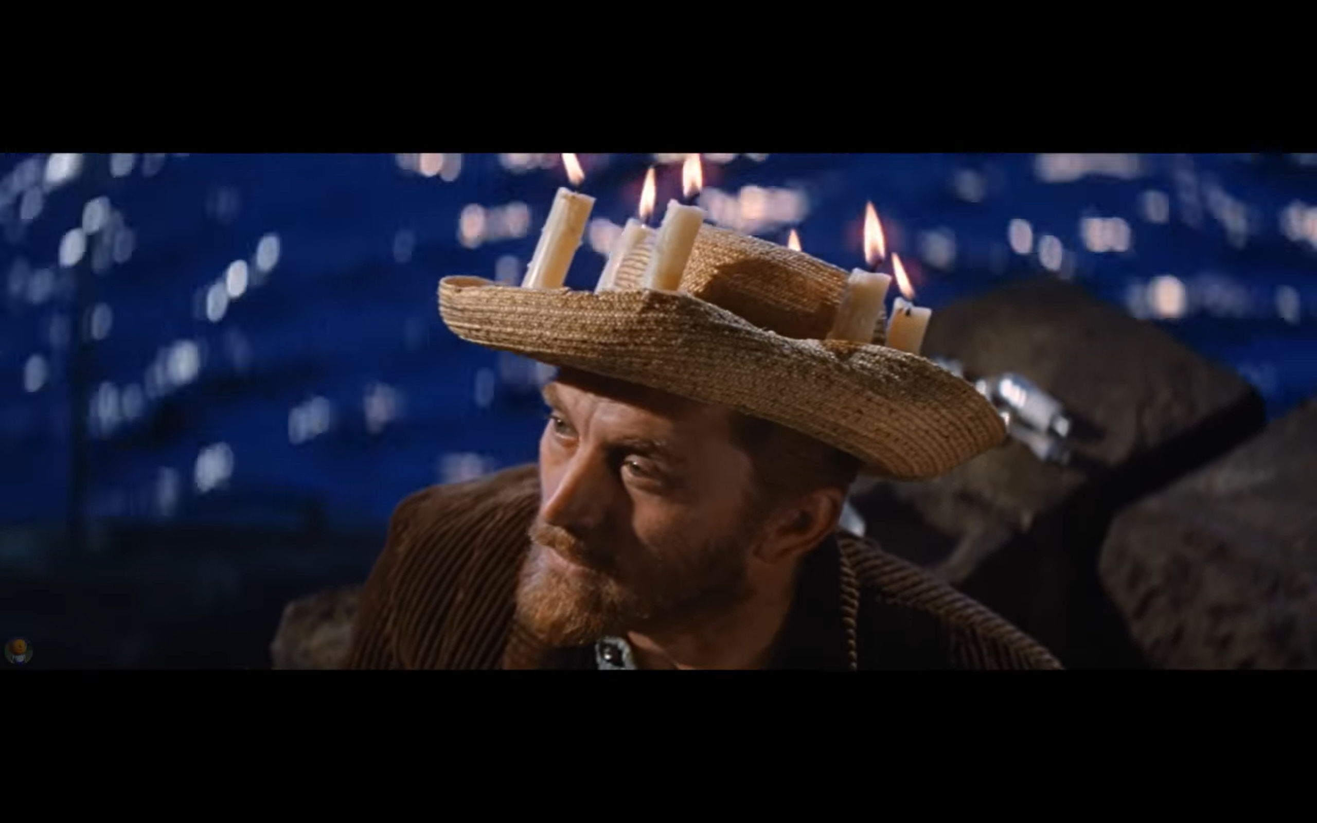 Film still of a Van Gogh character wearing a straw hat with candles against a dark background