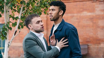 One teacher holds another back as he looks toward something off screen