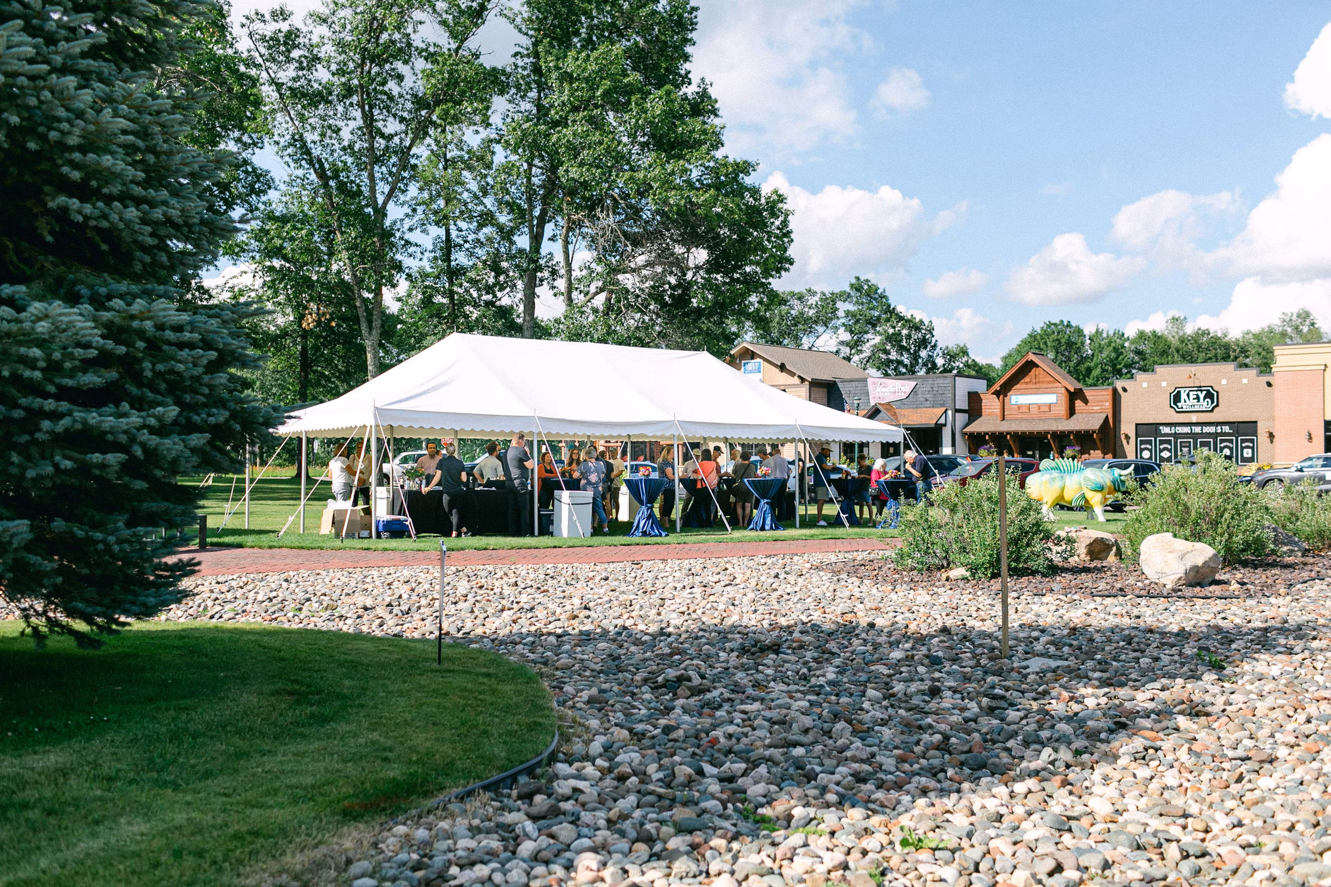 A crowd of people gathered beneath a pavillion type tent, in front of a strip mall but in a park-like area, apparently for some kind of celebration. They seem to be mostly (all?) white, which, frankly, tracks with mainline Protestants in the United States.