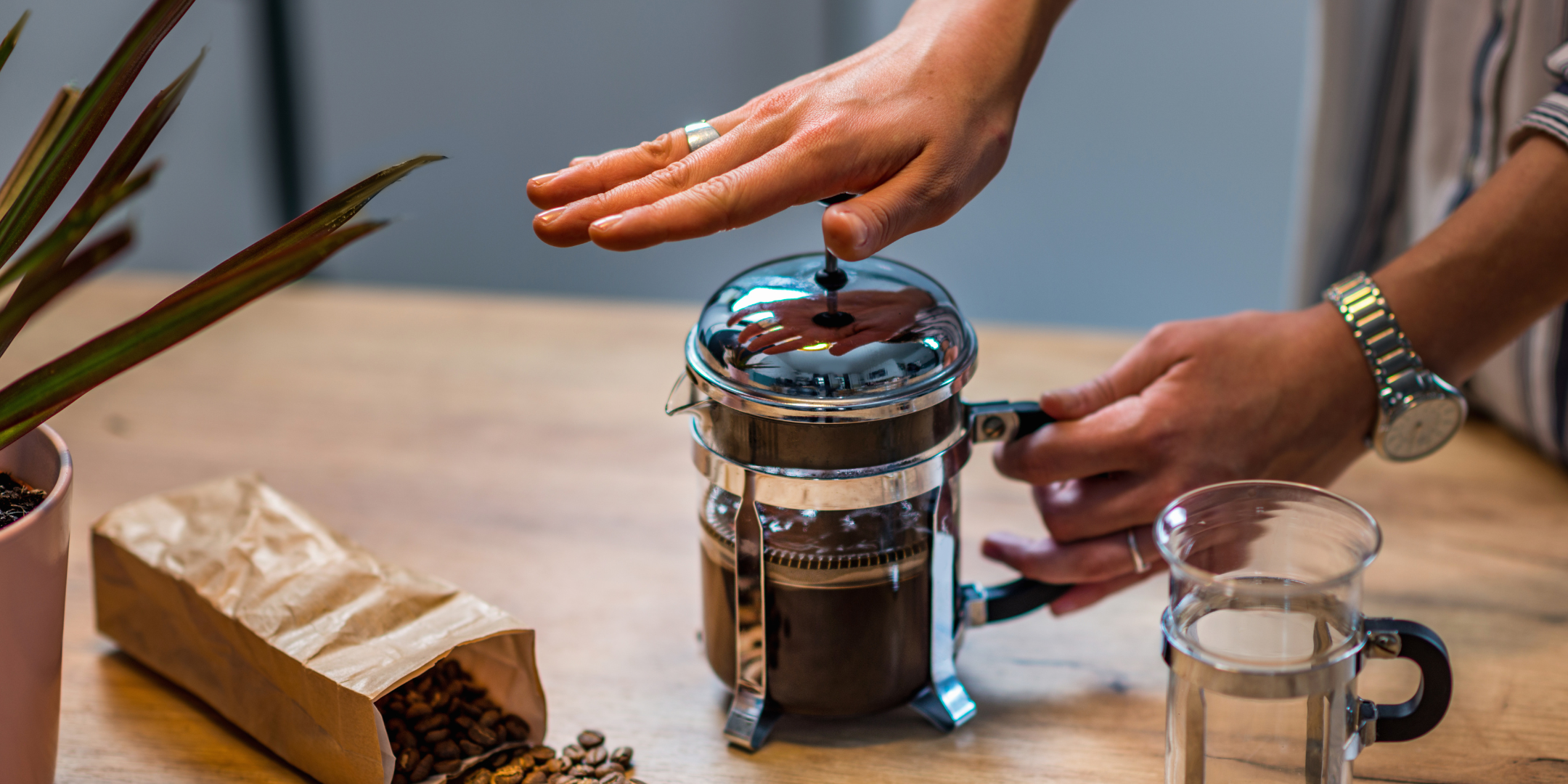 A close-up of a hand depressing the plunger of a coffee French press.