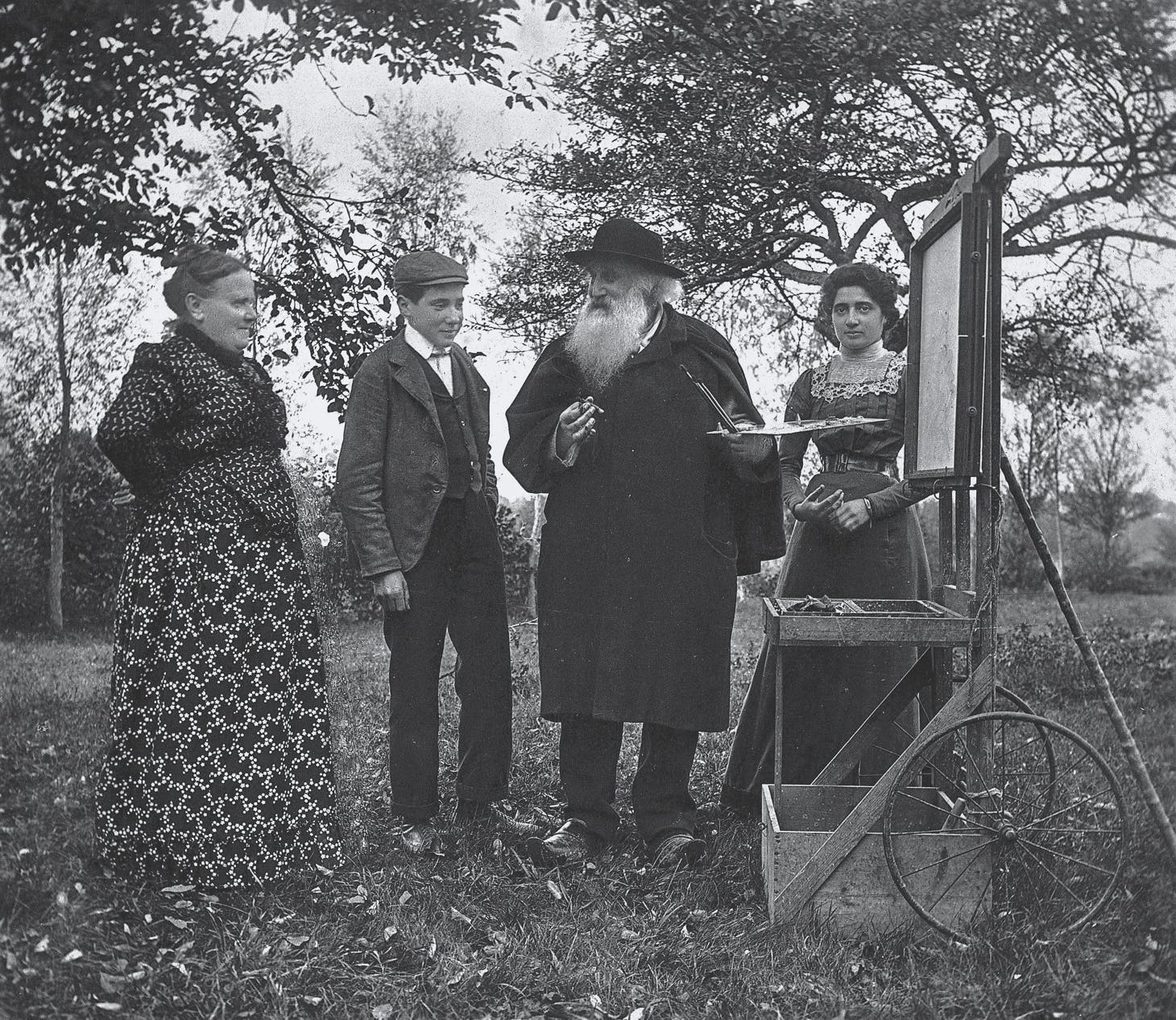 Historic photograph of four people beside an outdoor painter's easel