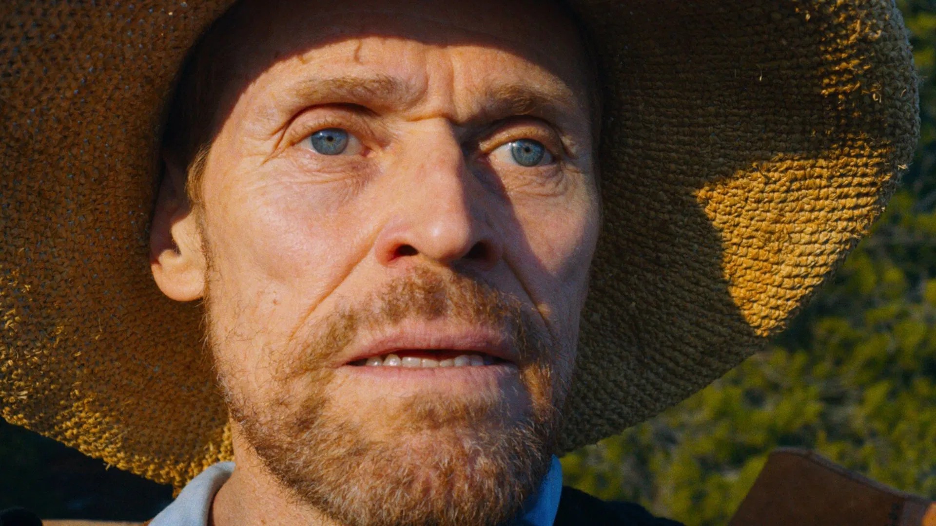 Close-up film still of Willem Dafoe as Van Gogh beneath a wide straw hat
