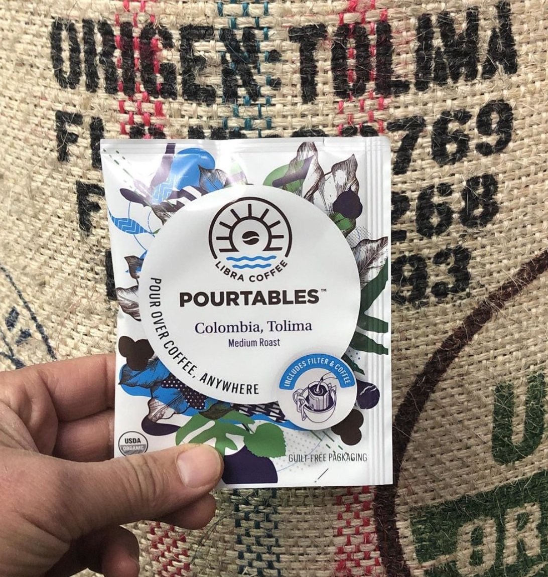 Libra Coffee's single serving pourtable package held up in front of a burlap coffee sack.