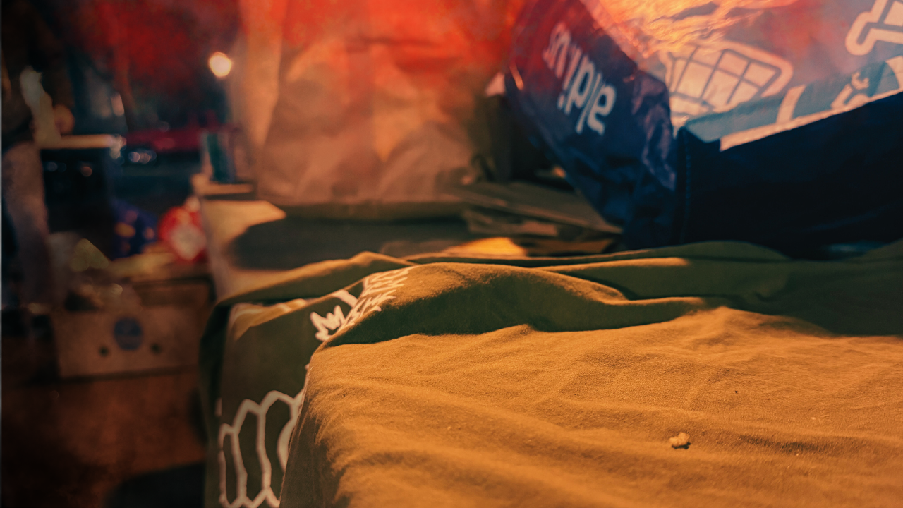 Close-up view of a wrinkled green fabric with various bags and items blurred in the background, illuminated with warm lighting.