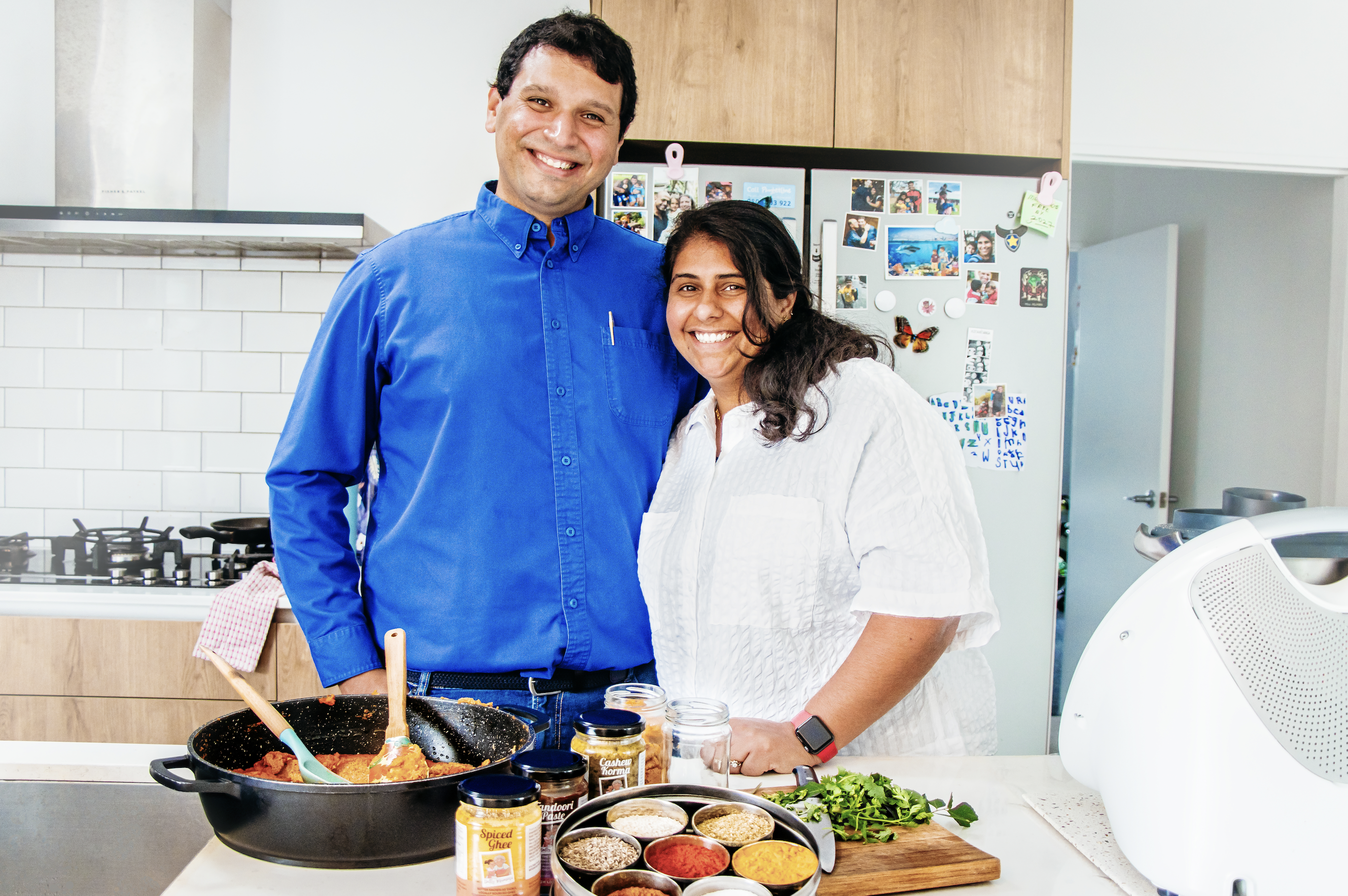 Perzen Patel and her husband in their kitchen with food on the counter top in front of them.