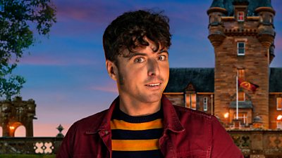 A young man in a black and yellow striped top and a red shirt looks nervously to camera, set against the backdrop of a castle by night