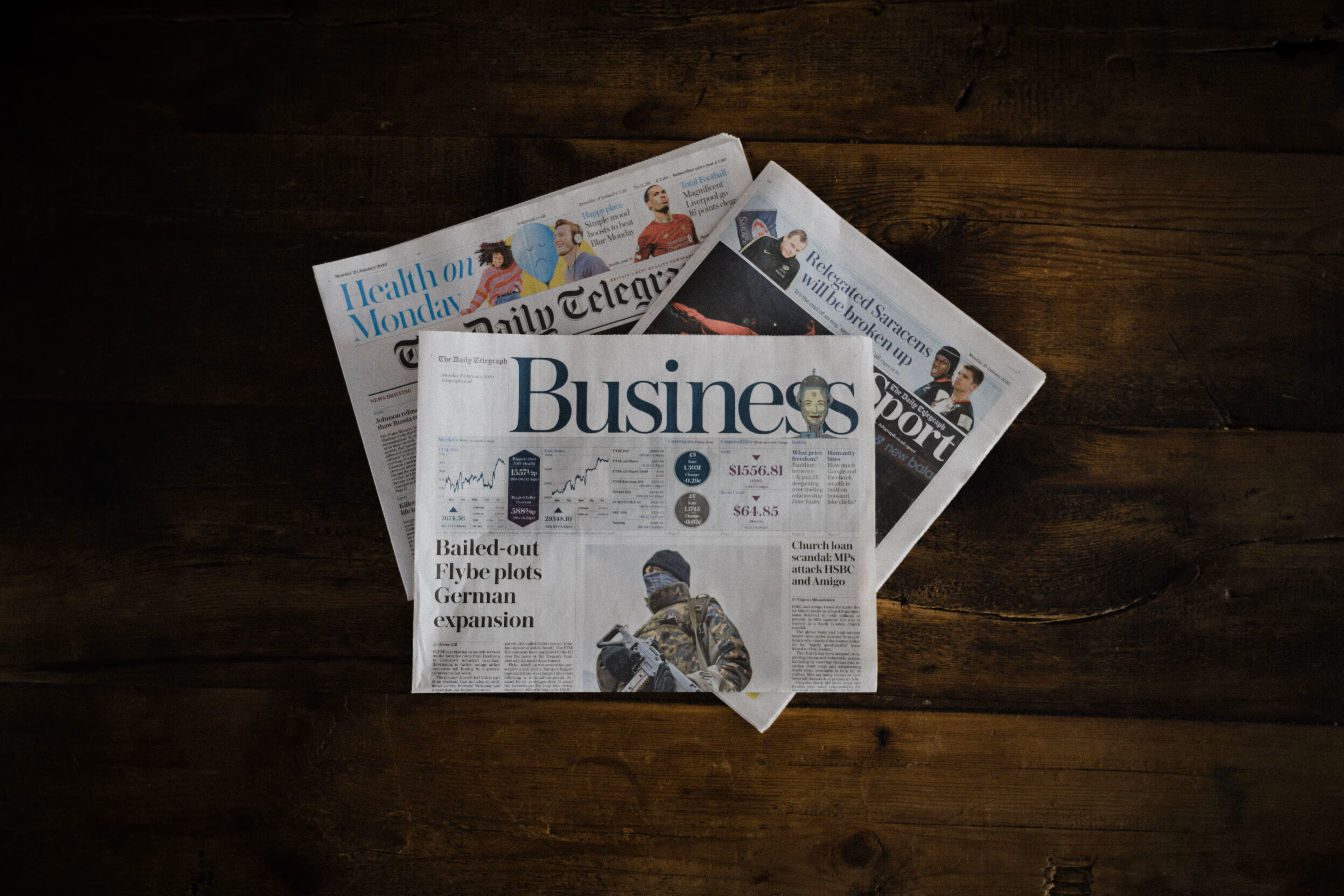 Newspapers spread across a wooden table, representing the overflow of information and the challenge of meaning in the AI content era.