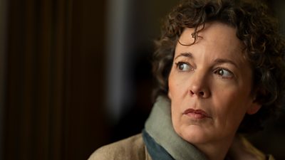 A woman with short curly hair in pictured in profile looking over her shoulder at something off screen