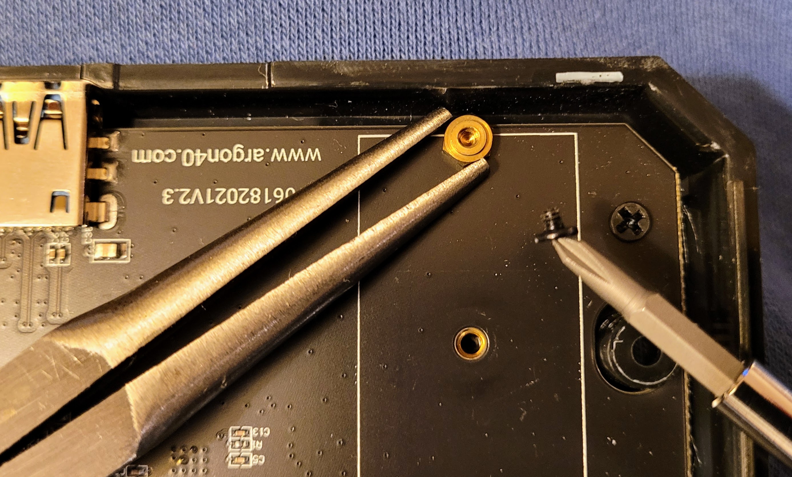 The brass screw is mounted to the SSD interface and the black screw then secures the SSD