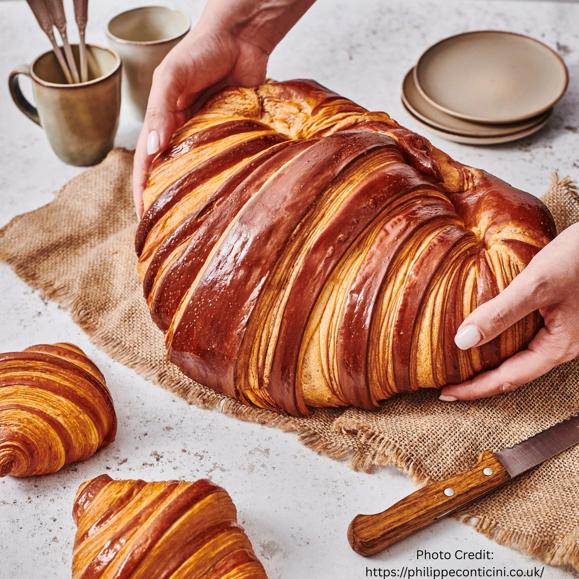 Oversized croissant held in two hands beside smaller croissants