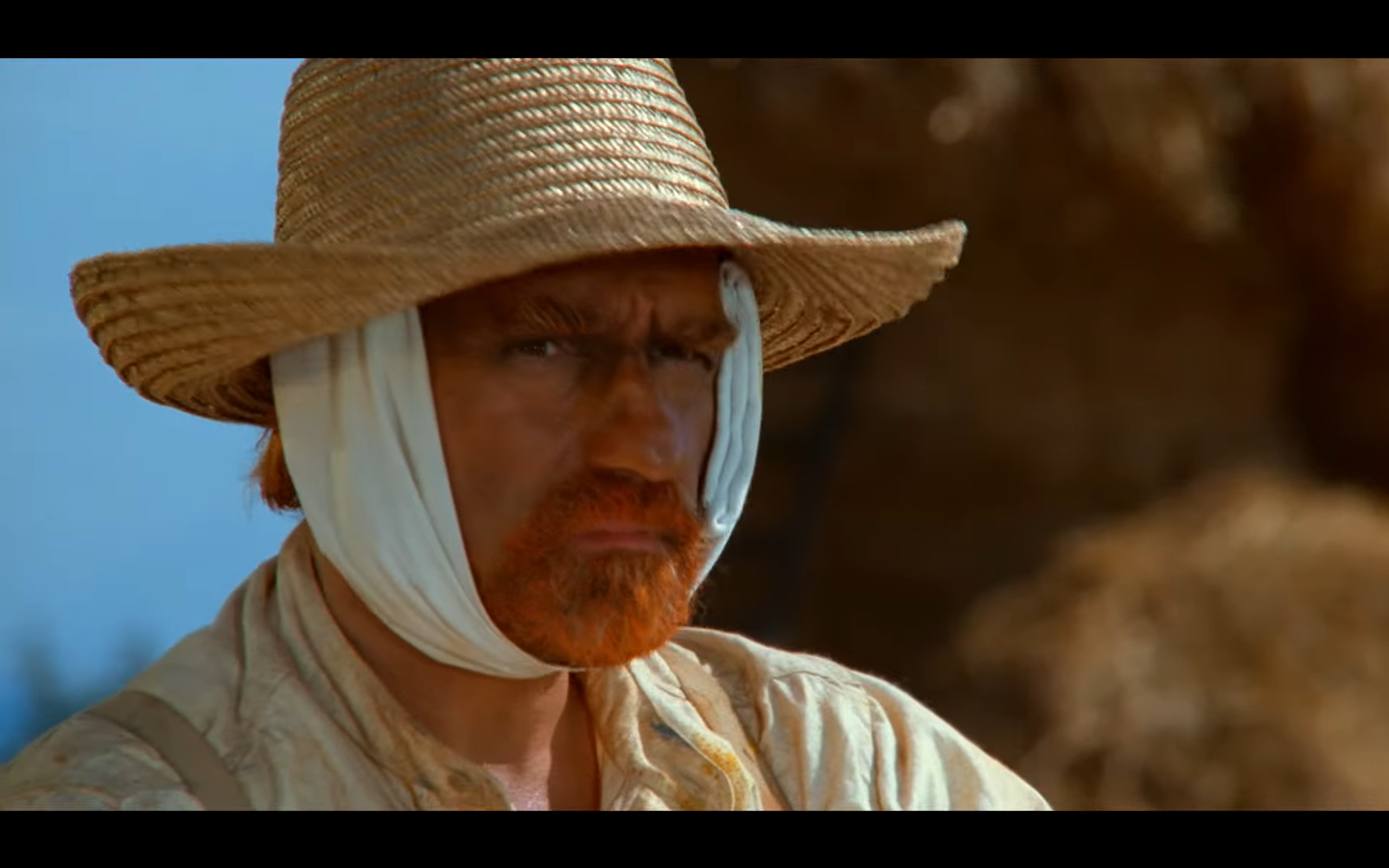 Film still of Willem Dafoe as Van Gogh wearing a straw hat and ear bandage
