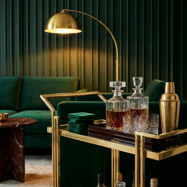 Neo Deco brass bar cart with crystal decanters and emerald velvet accents in a moody living room