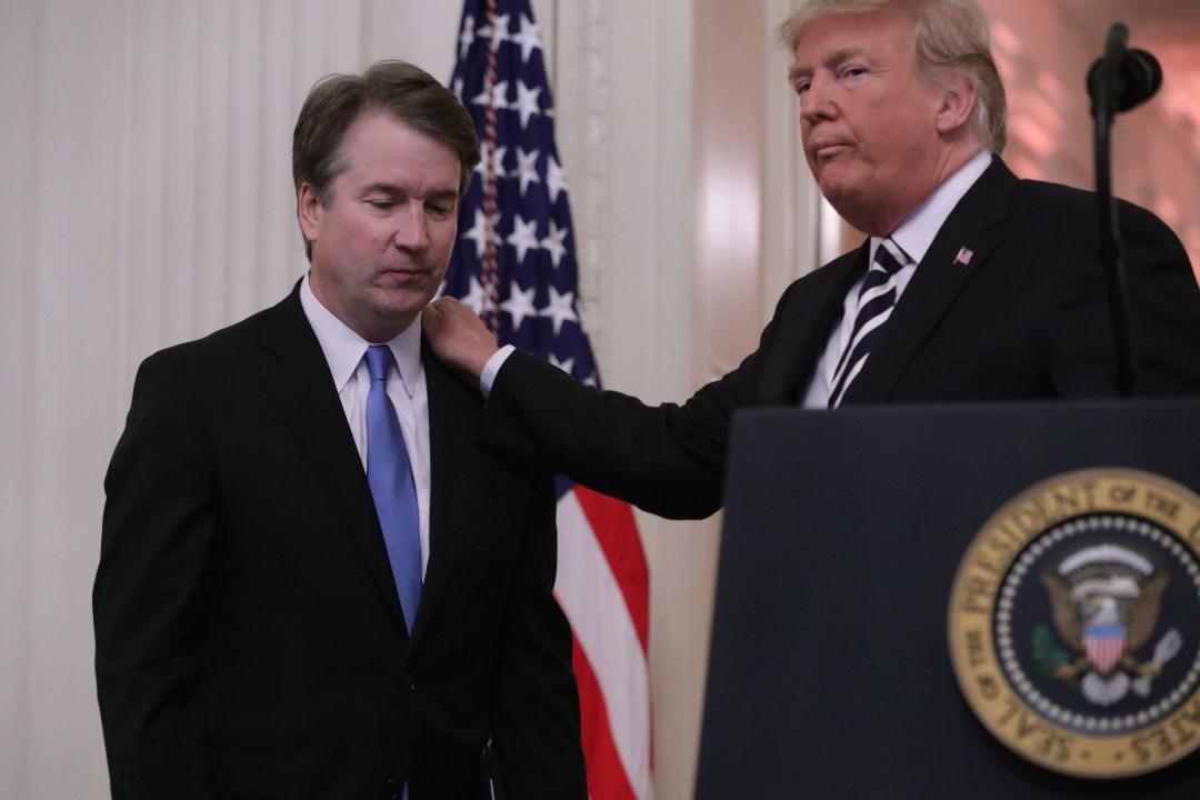 A man rests a hand on the shoulder of another man in a suit at a podium.