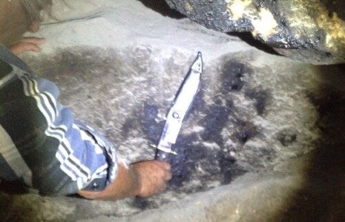 a man holding a knife in a cave next to an imprint of a hand