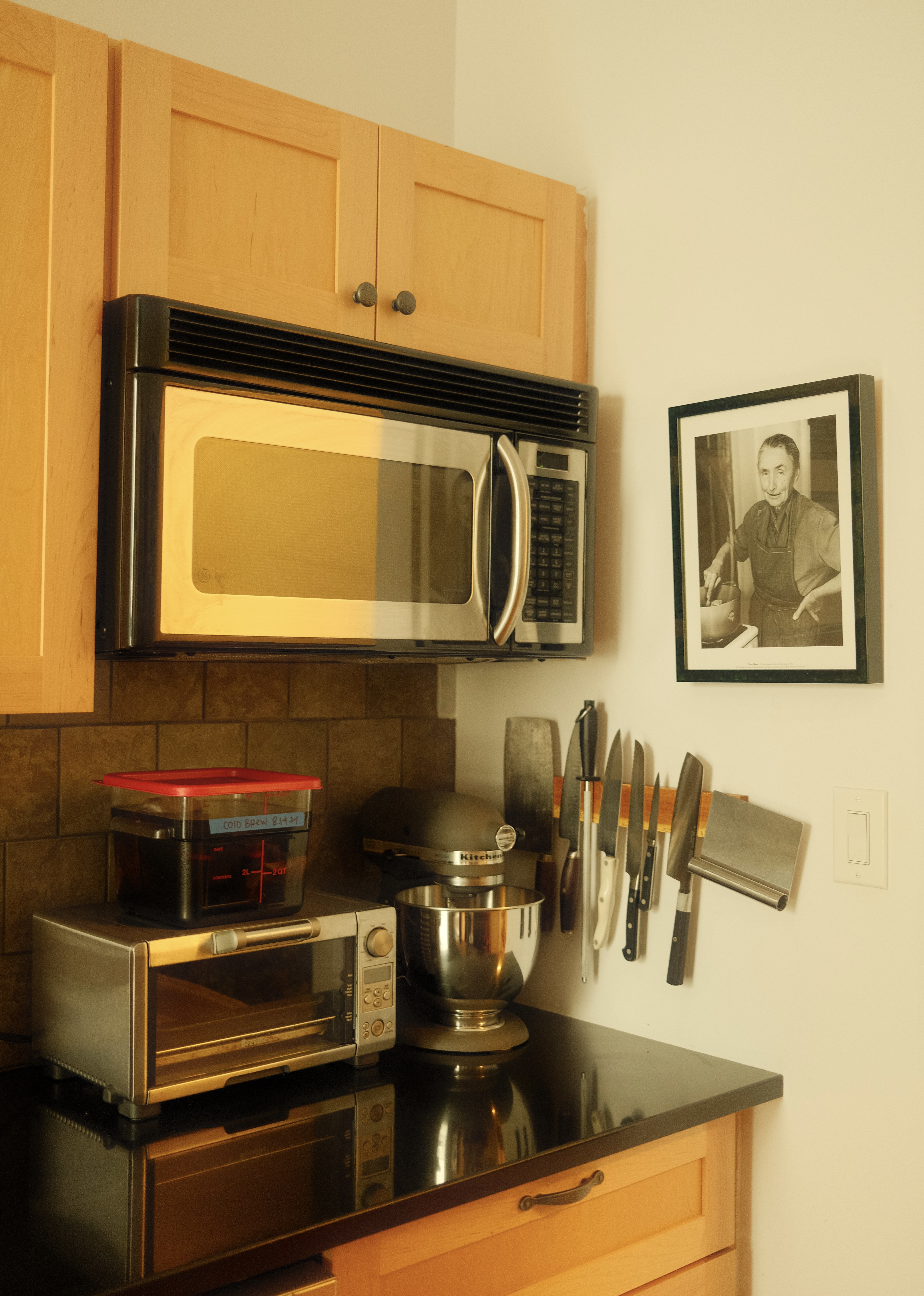 Kitchen gadgets on a counter top. Microwave fixed to the wall under wooden cupboards. Kitchen gadgets on a counter top. Microwave fixed to the wall under wooden cupboards.