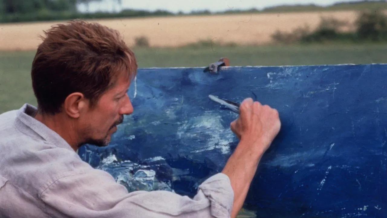 Film still of an actor portraying Van Gogh painting a blue canvas outdoors