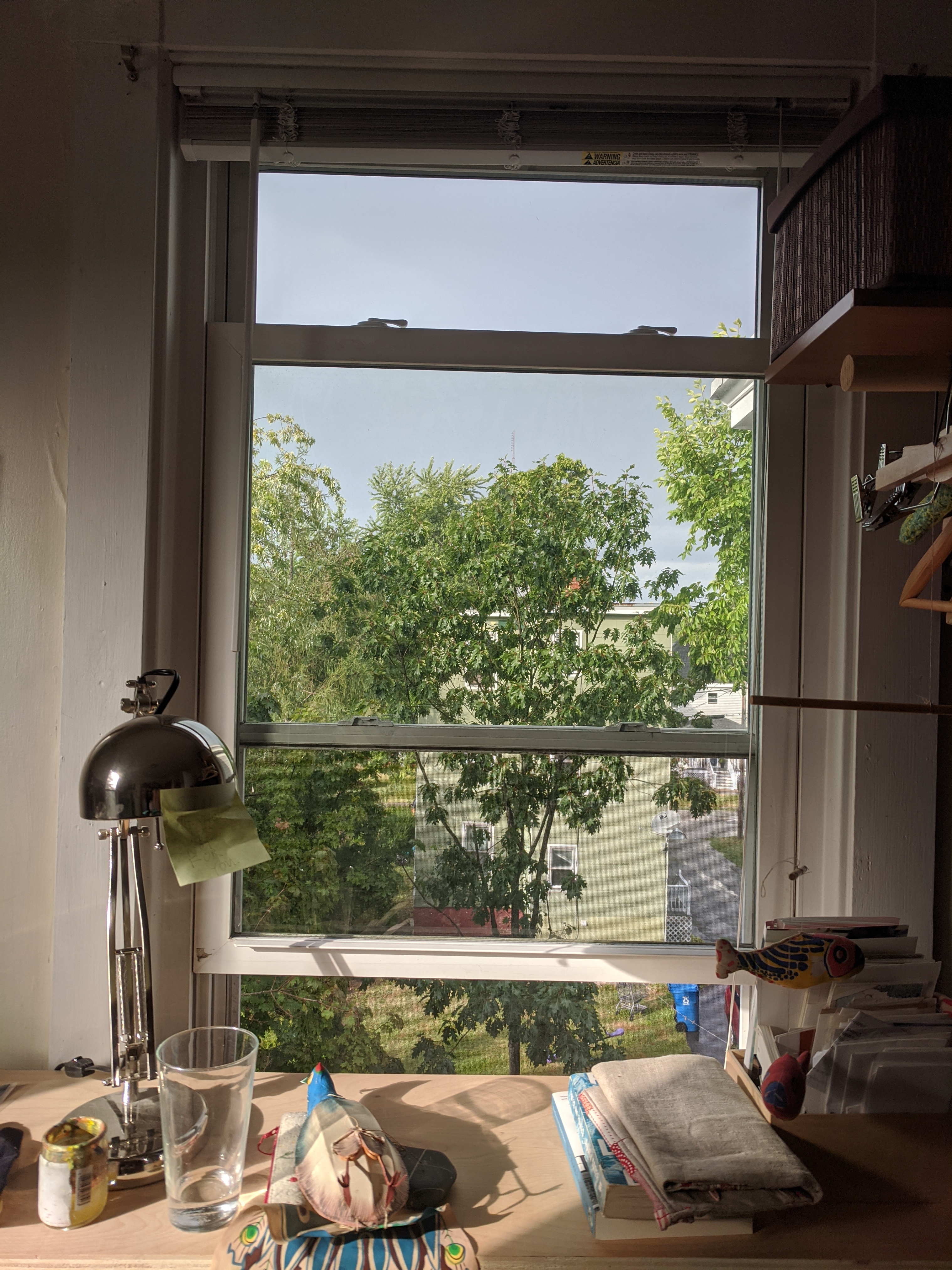 An open window in front of which there is a desk with bits and pieces of household things on it.