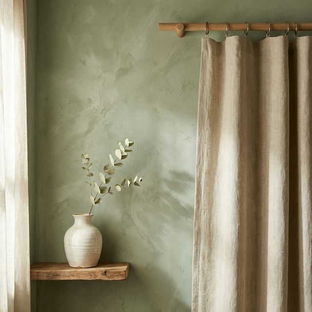 Sage green limewash wall detail with raw linen curtain and ceramic vase
